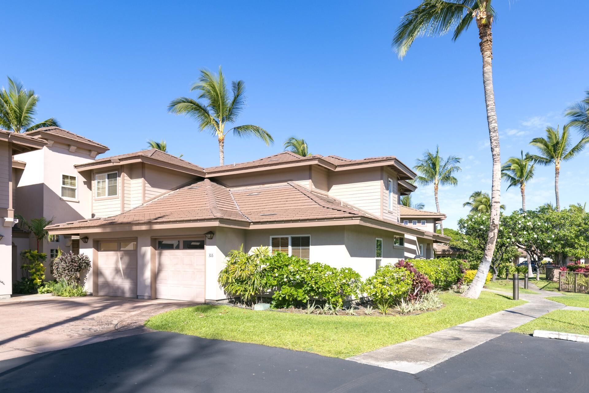 A two-story residential house with a garage, surrounded by well-maintained lawns and palm trees.