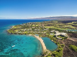 Vista aérea de un complejo turístico frente al mar con propiedades en la playa, un campo de golf y un gran conjunto de edificios.