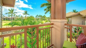 A balcony with a view of a tropical landscape, including palm trees and a building in the background. - Waikoloa Colony Villas Resort by KBM (Waikoloa)