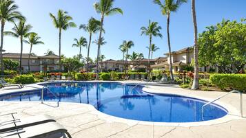 Piscina com espreguiçadeiras, rodeada por palmeiras e um edifício residencial.