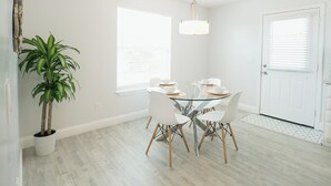 Un comedor con una mesa redonda de cristal, sillas blancas y una lámpara colgante.