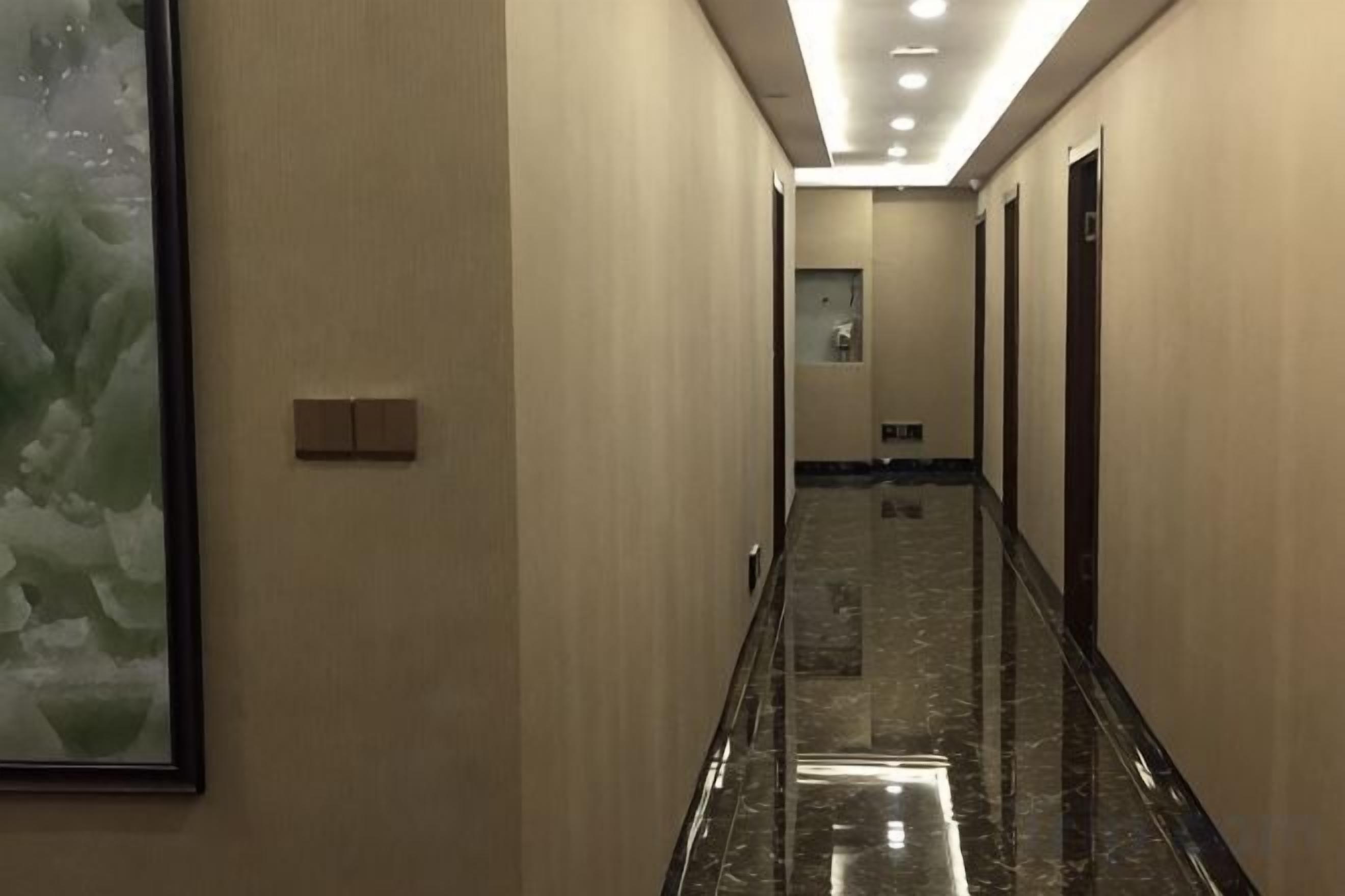 A hallway with a marble floor, doors on both sides, and a light switch on the wall.
