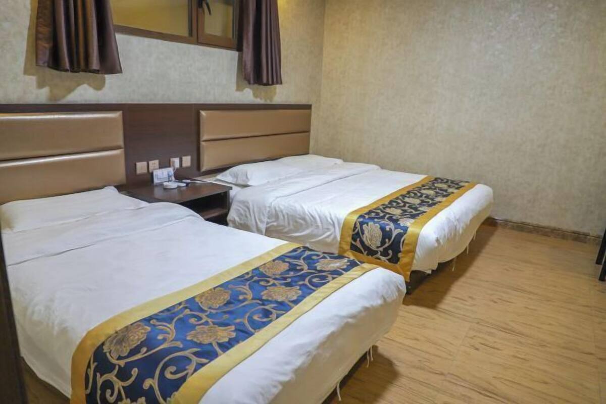 A hotel room with two beds, a nightstand, a mirror, and a wooden floor.