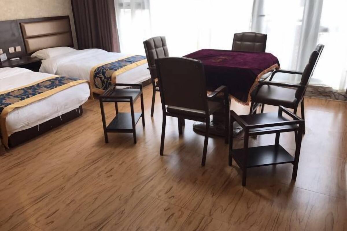 A hotel room with two beds, a dining table with four chairs, and a large window.