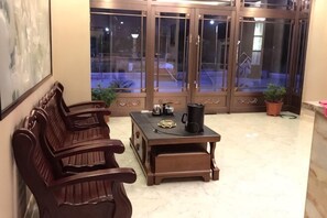A seating area with wooden benches, a table with a coffee pot, and a view through glass doors. - Yida Hotel (Changbai Mountain West Slope Tourist Transfer Center) (Fusong)