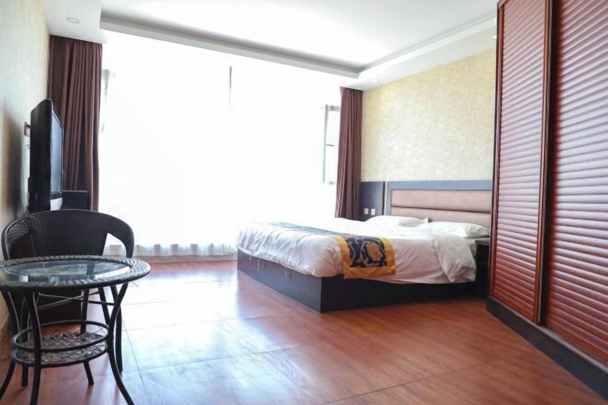 A hotel room with a bed, a chair, a table, and a large window.
