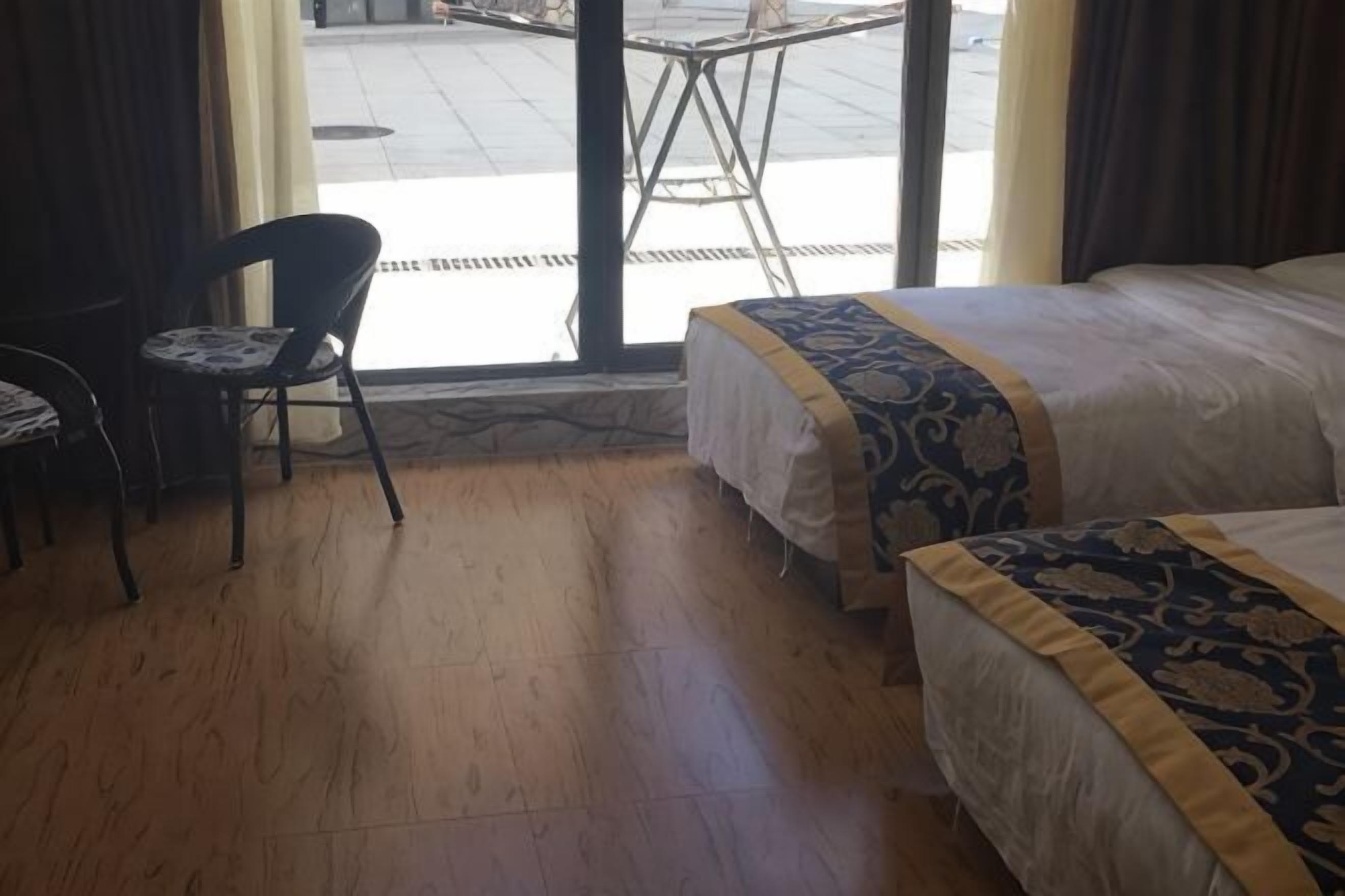 Una camera d'albergo con due letti, una sedia e vista sulla strada attraverso una porta vetrata.