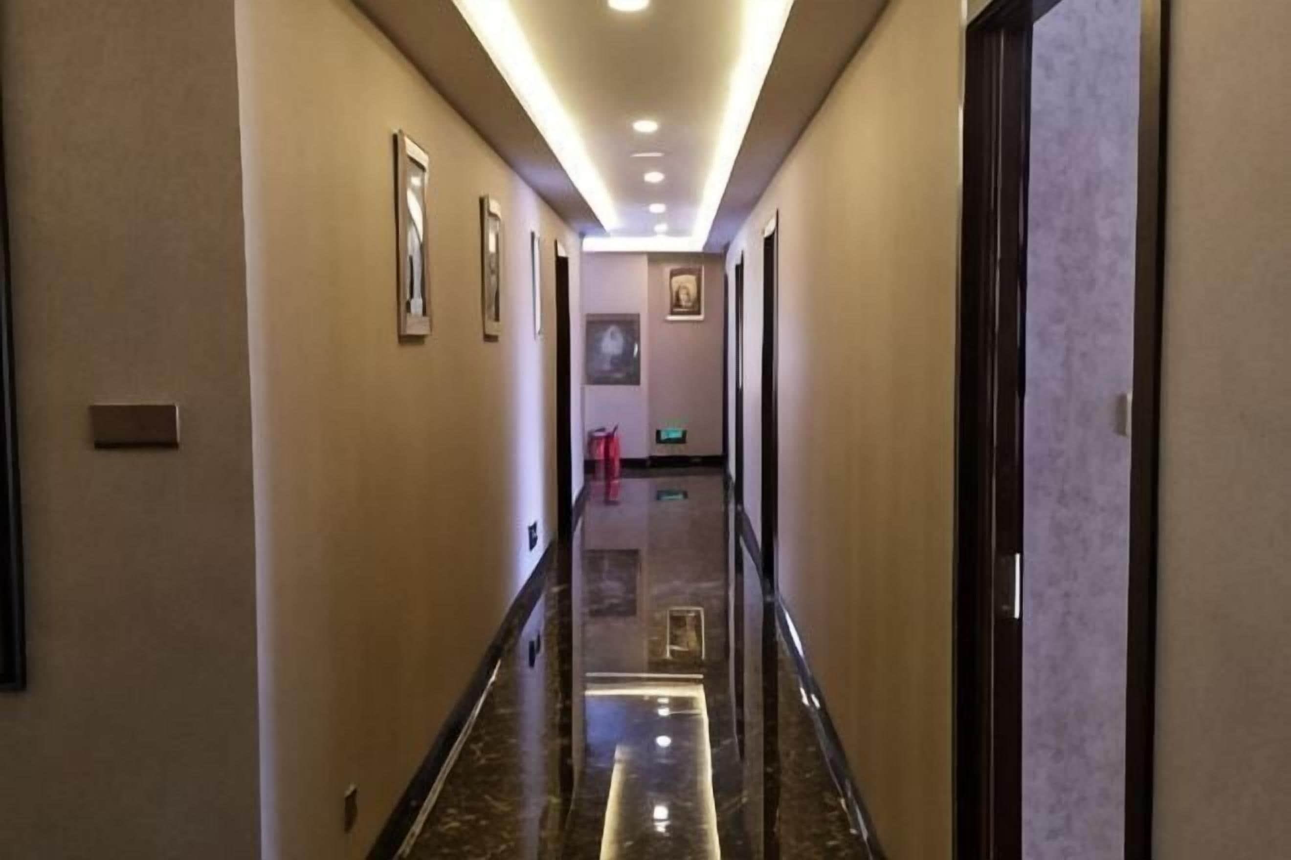 A hotel hallway with framed pictures on the walls, a polished floor, and a door at the end.