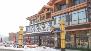 A hotel with a large sign, outdoor seating, and snow on the ground. - Yida Hotel (Changbai Mountain West Slope Tourist Transfer Center) (Fusong)