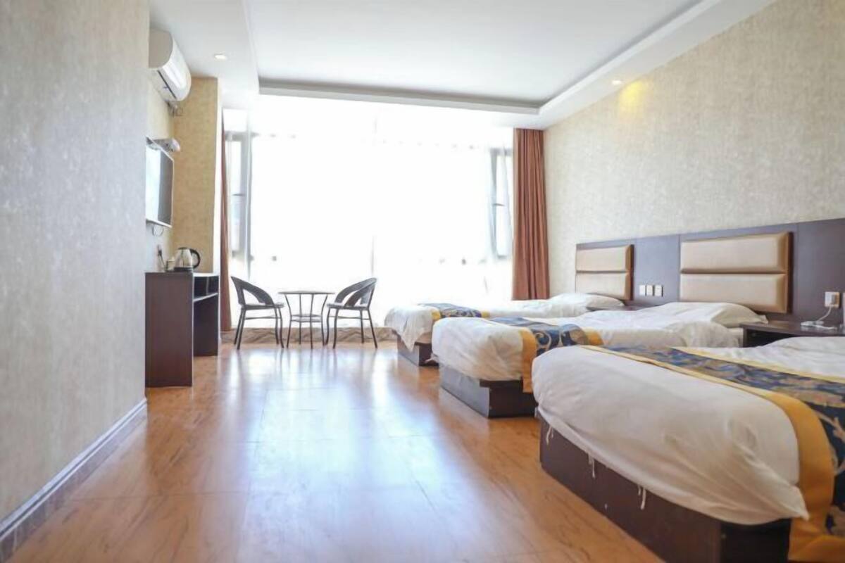 A hotel room with two beds, a desk, a chair, and a large window.