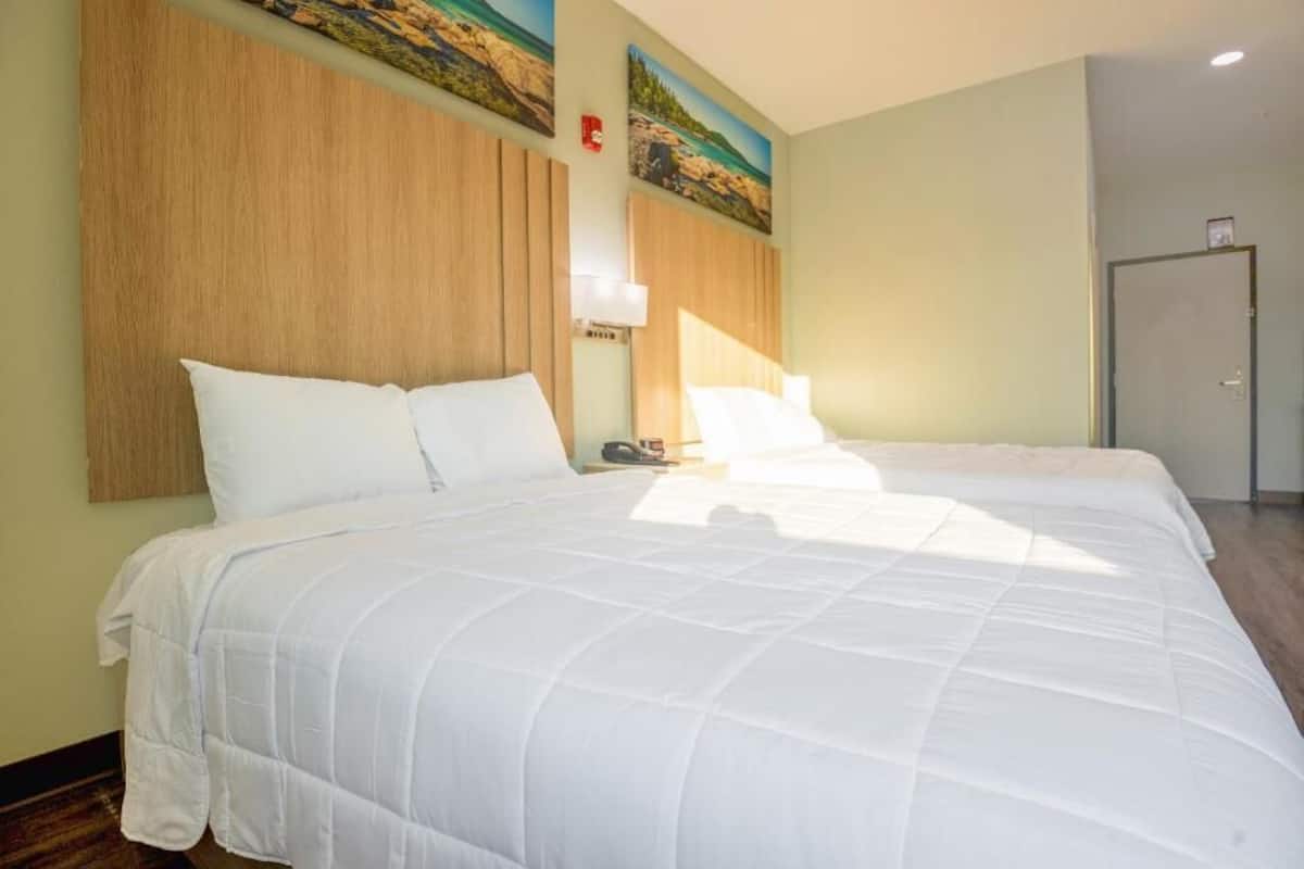 A hotel room with two beds, wooden headboards, and a painting on the wall.
