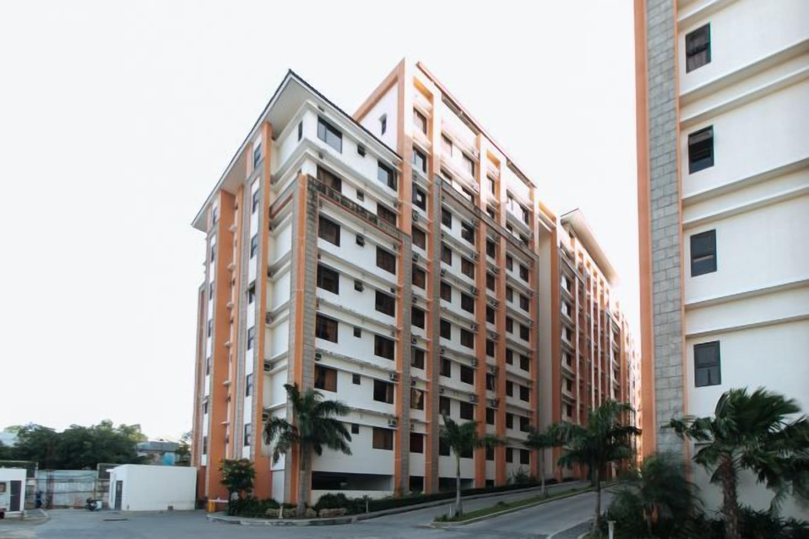Een meerlaags woongedeelte met een modern architectuurontwerp, met een combinatie van witte en oranje gevels, omgeven door palmbomen.