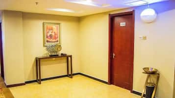 A hotel hallway with a wooden door, a console table with a vase, and a wall-mounted light fixture.
