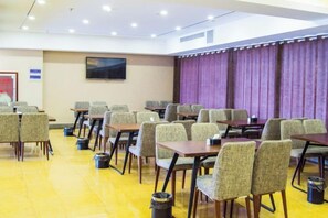 A conference room with rows of tables and chairs, a television screen on the wall, and a purple curtain backdrop. - Bali Hotel (Cao County)