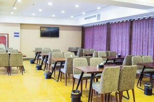 Un salón de conferencias con filas de mesas y sillas, una pantalla de televisión en la pared y un telón de fondo morado.