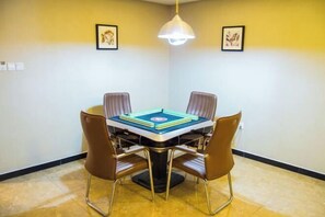 A dining area with a square table surrounded by four chairs, a hanging light fixture, and two framed pictures on the walls. - Bali Hotel (Cao County)