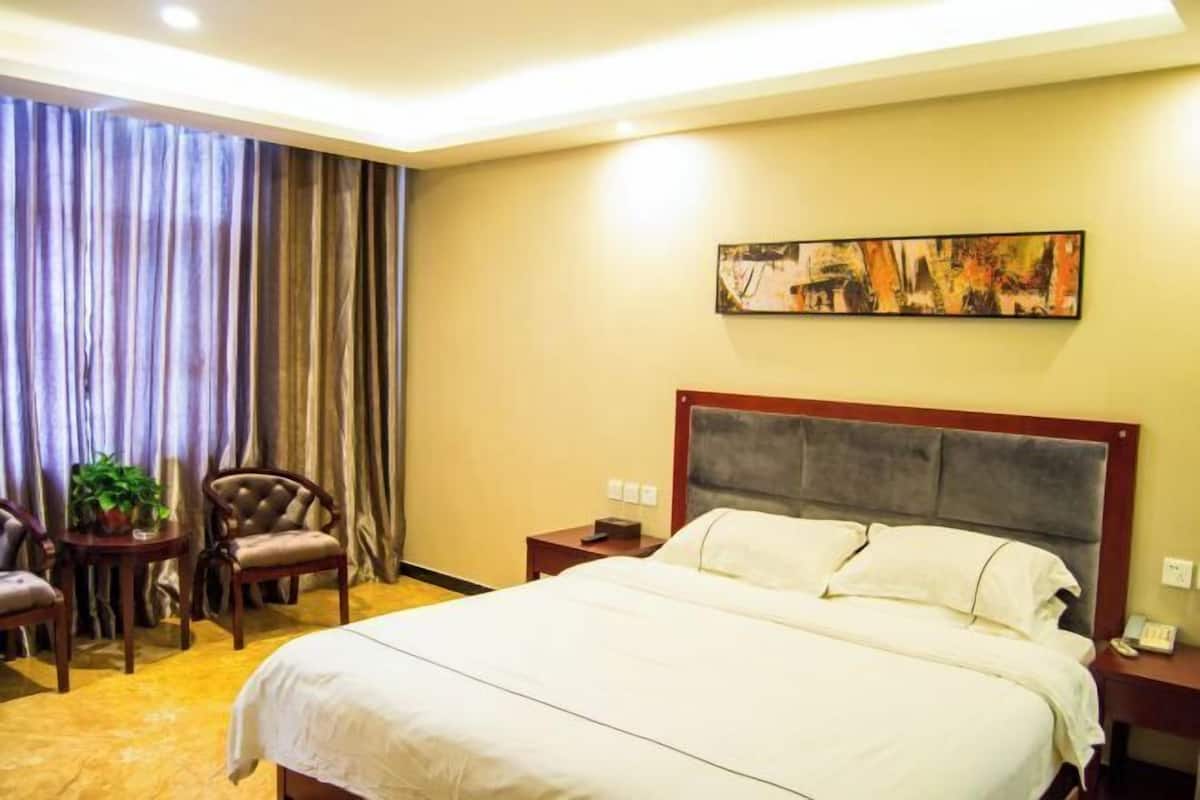 Une chambre d’hôtel avec un grand lit, une table de chevet, une chaise, une petite table avec une plante et un tableau au mur.