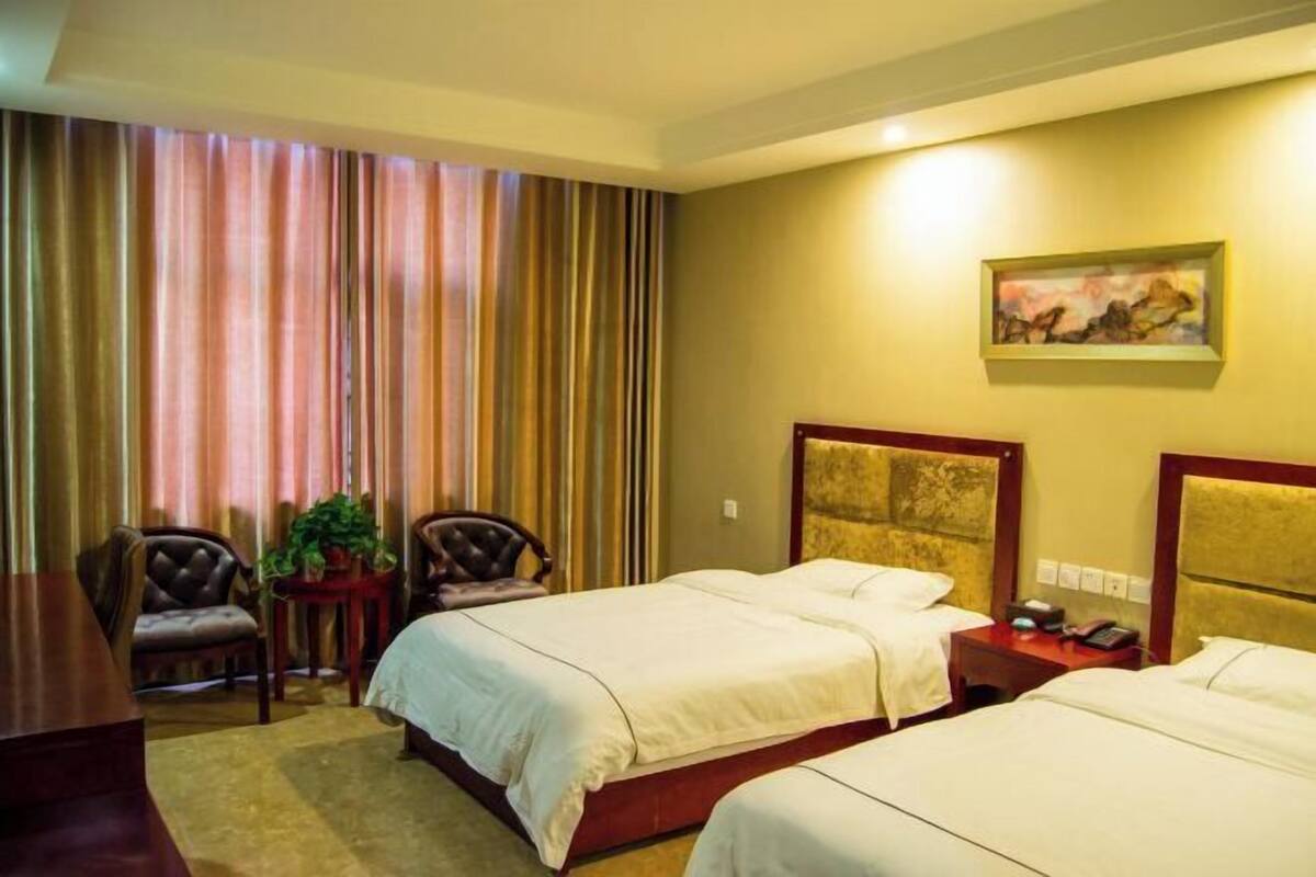 Une chambre d’hôtel avec deux lits, un bureau, une chaise, une petite table avec une plante et un tableau au mur.