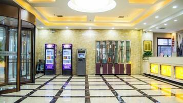 A lobby with a check-in counter, vending machines, a glass elevator, and a marble floor.