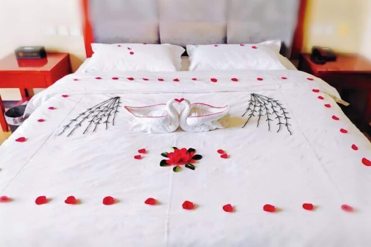 Un lit parsemé de pétales de rose et orné d’un motif de cygne, une table de chevet rouge et une tête de lit blanche.