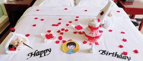 A bed with a white bedspread, red rose petals, and a birthday decoration.