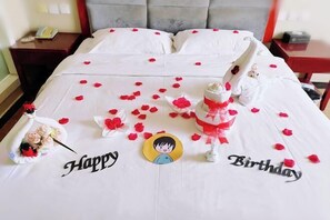 A bed with a white bedspread, red rose petals, and a birthday decoration. - Bali Hotel (Cao County)