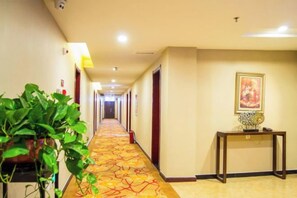 Un pasillo de hotel con piso alfombrado, puertas a ambos lados, una mesa con un florero y una planta en maceta.