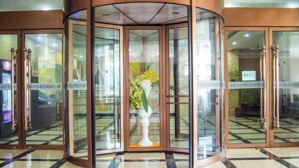 A revolving door with glass panels and a white vase with flowers in the center.