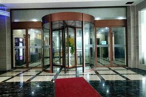 A revolving door with glass panels, a red carpet, and a check-in counter to the left. - Bali Hotel (Cao County)