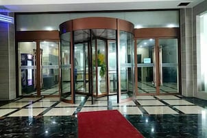 A revolving door with glass panels, a red carpet, and a check-in counter to the left.