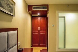 A hotel room with a wooden wardrobe, a bed with a headboard, a small table, and a window with blinds. - Bali Hotel (Cao County)