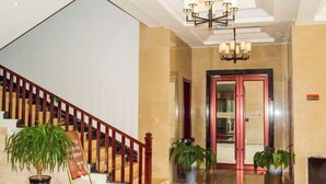 A hotel lobby with a staircase, a chandelier, and potted plants.