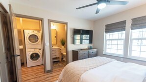 Une chambre à coucher comprenant un lit, un ventilateur de plafond, une fenêtre avec des stores, une commode, un miroir et une buanderie équipée d’un lave-linge et d’un sèche-linge.