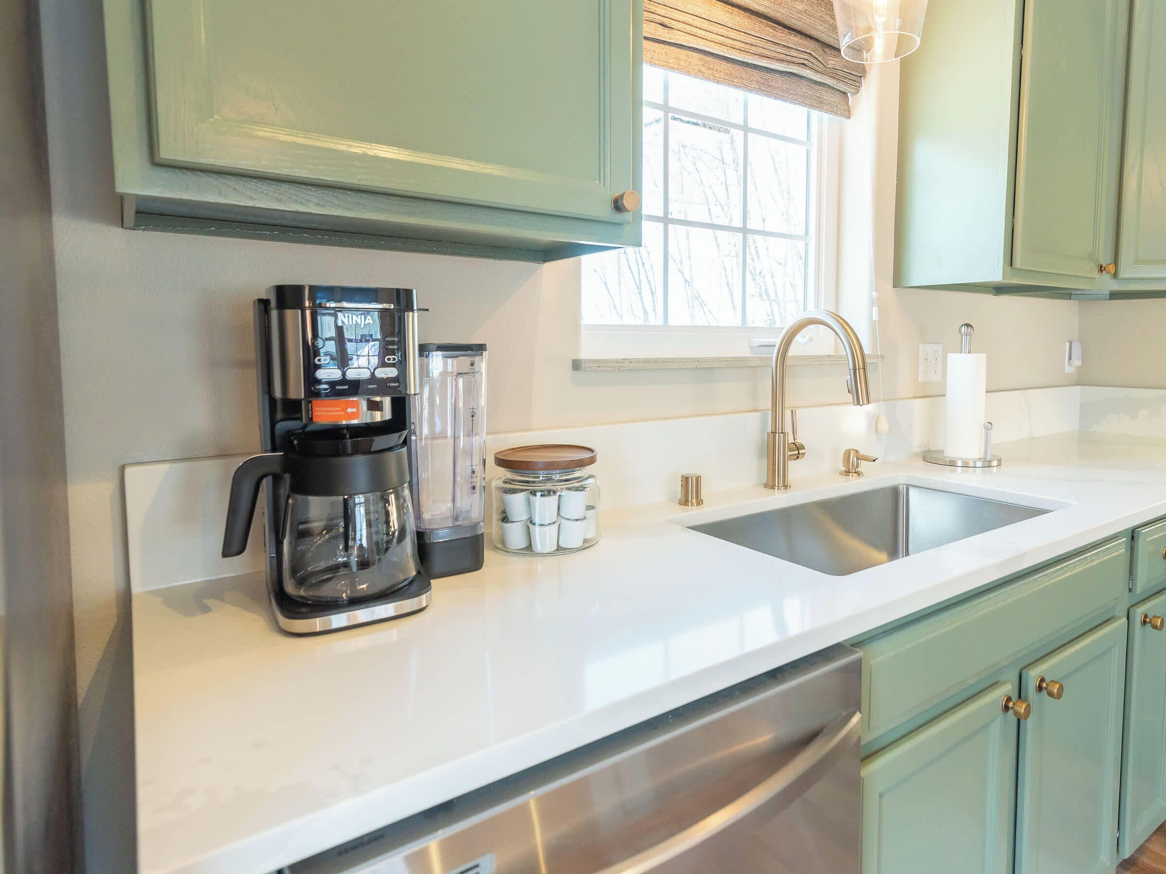 A kitchen with a coffee maker, a blender, a jar of spices, and a sink.