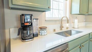 A kitchen with a coffee maker, a blender, a jar of spices, and a sink.