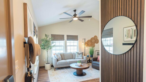 Un salon avec un ventilateur de plafond, un miroir rond, un canapé, une table basse et une plante en pot.