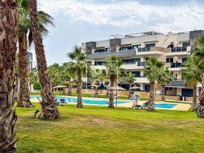 A modern hotel with multiple balconies, a swimming pool, and palm trees.