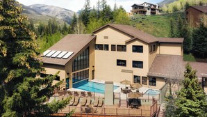 Un edificio moderno de dos pisos con una amplia piscina, mobiliario exterior y vistas a las montañas.