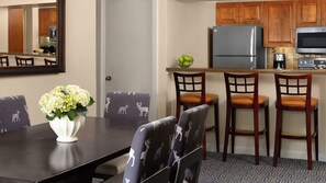 Un coin repas avec une table, des chaises et un vase de fleurs. La cuisine est équipée de meubles en bois et d’appareils électroménagers.