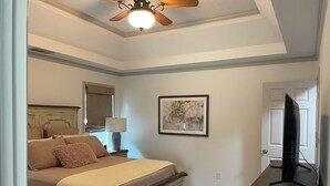 A bedroom with a bed, a ceiling fan, a TV, a lamp, and a framed picture on the wall.