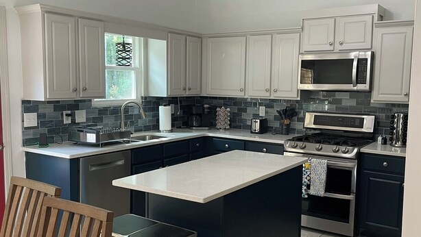 A modern kitchen with white cabinets, a central island, stainless steel appliances, and a ceiling fan.