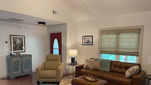 A living room with a brown leather sofa, a beige armchair, a patterned rug, and a small side table with a lamp.