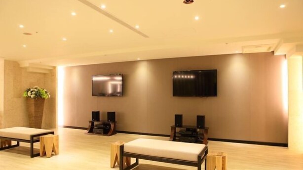 Amplia habitación con suelo de madera, un banco, dos altavoces y un televisor de pantalla plana montado en la pared.