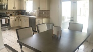 Een moderne keuken met witte kasten, een eettafel met stoelen en een groot raam dat voor natuurlijk licht zorgt.