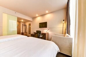 Une chambre d’hôtel avec deux lits, un bureau, une chaise, un miroir et une fenêtre avec des rideaux.