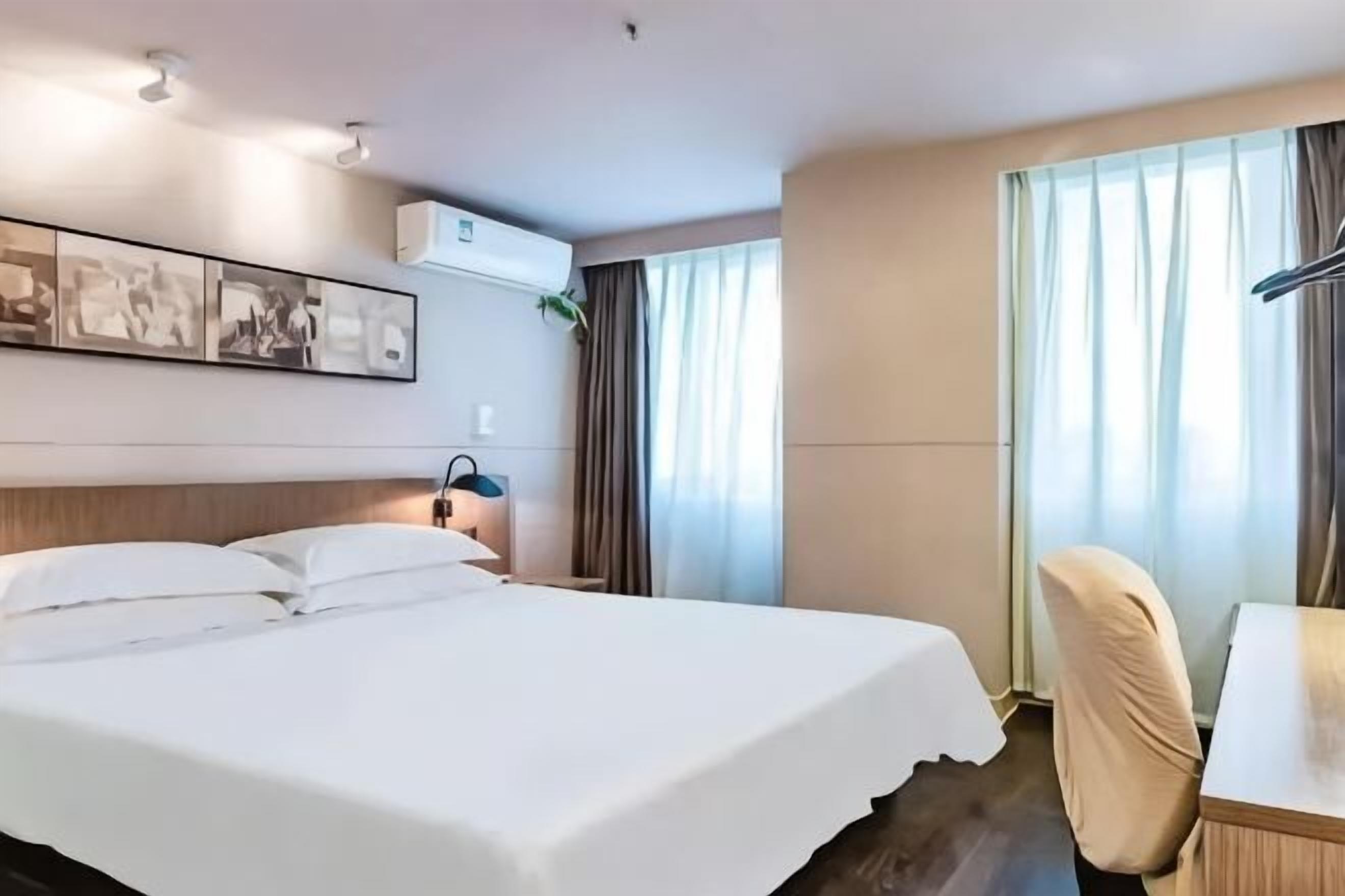 A hotel room with a bed, a desk, a chair, and a window with curtains.