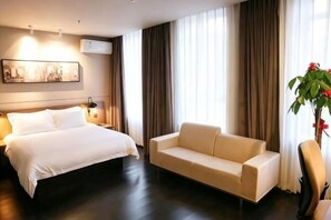 Une chambre d’hôtel avec un lit, un canapé, une chaise, une plante et un tableau au mur.