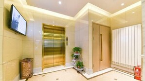 Um hall moderno com piso de mármore, uma tela digital, um elevador dourado e um extintor de incêndio.