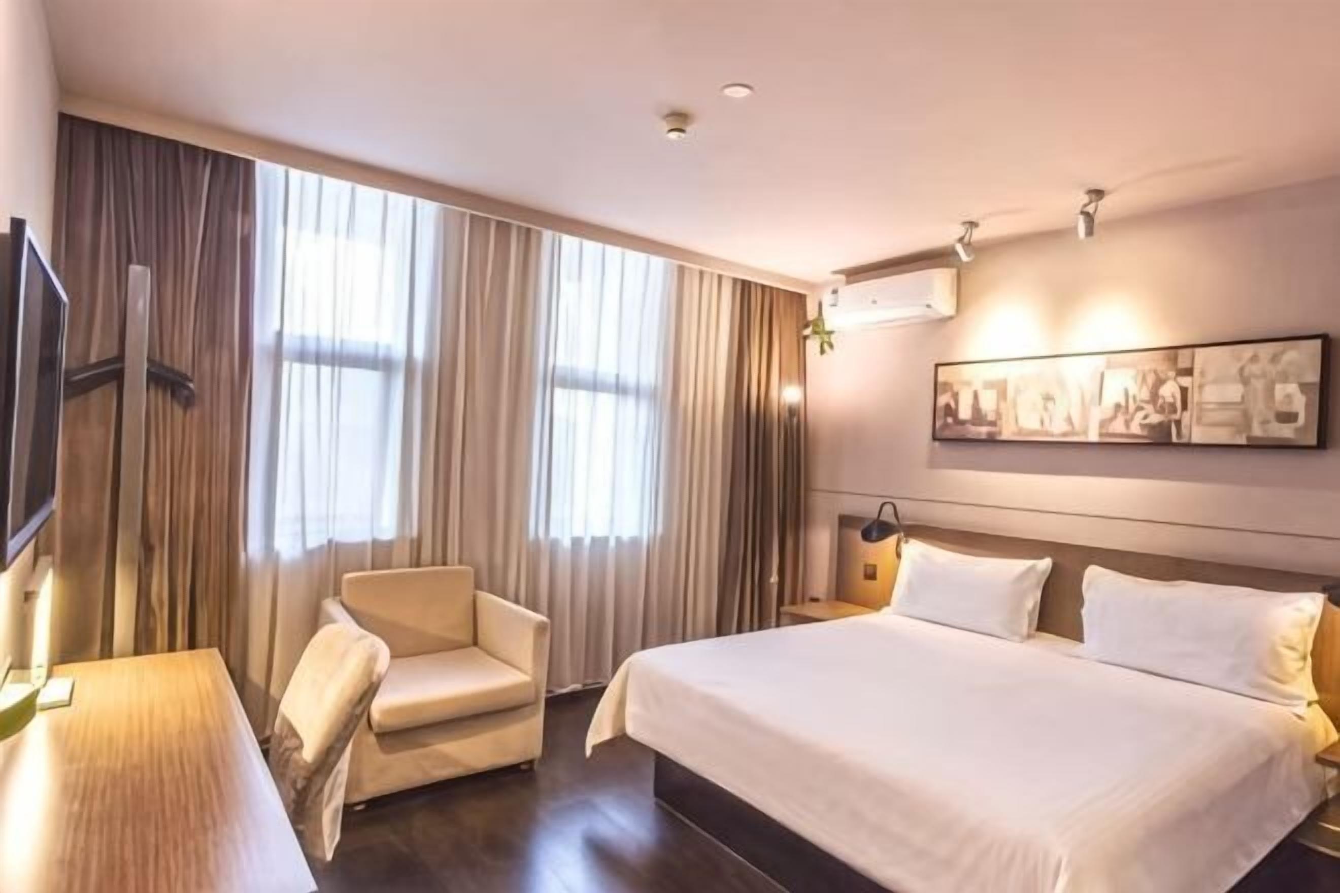 A hotel room with a large bed, a chair, a desk, and a television.