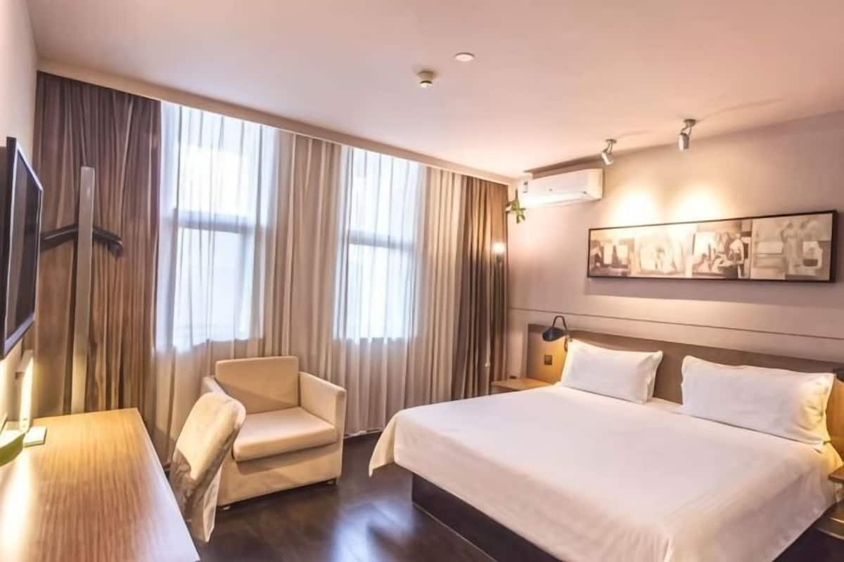 A hotel room with a large bed, a chair, a desk, and a television.